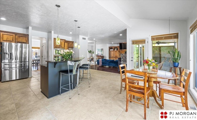kitchen with a center island, a kitchen bar, dark countertops, brown cabinetry, and stainless steel refrigerator with ice dispenser