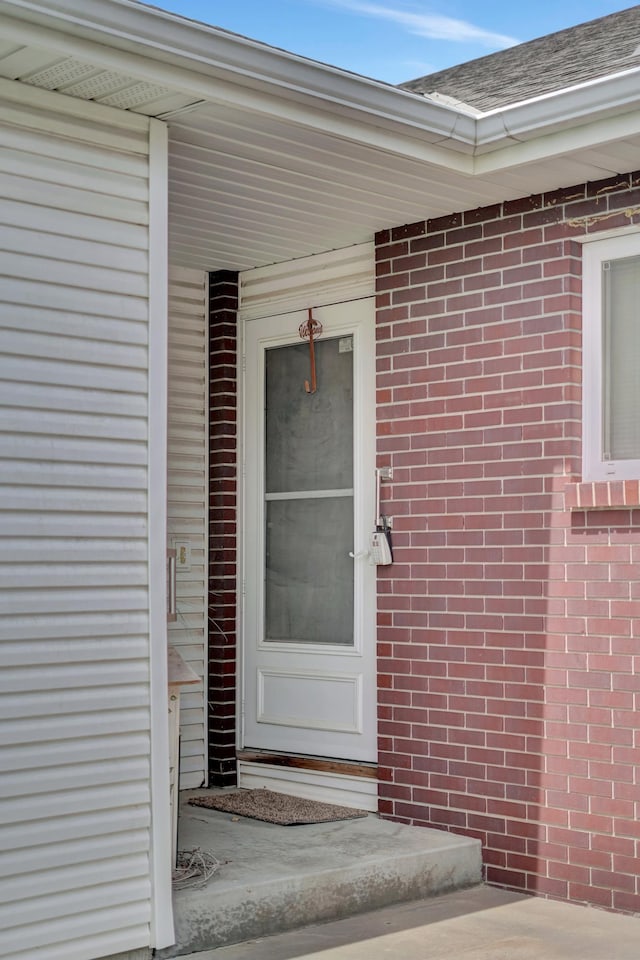 view of exterior entry featuring brick siding and roof with shingles
