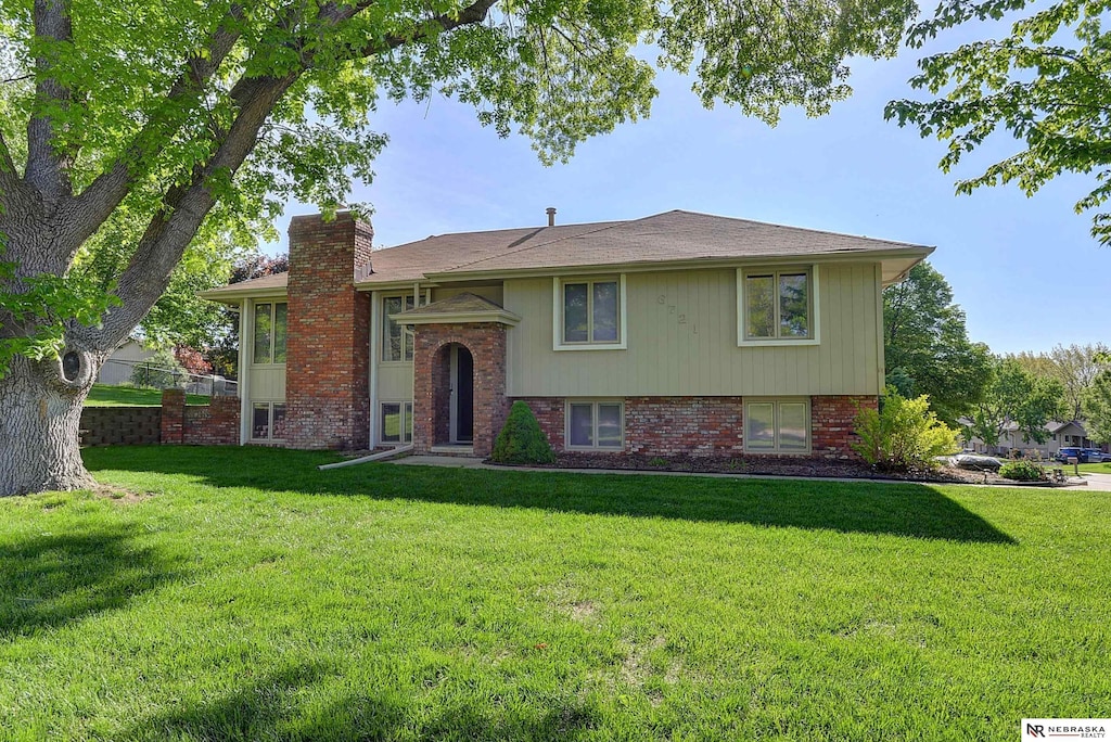 split foyer home with a front yard, a chimney, and brick siding