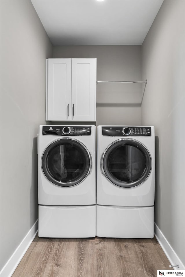 clothes washing area featuring washing machine and clothes dryer, cabinet space, baseboards, and light wood-style floors