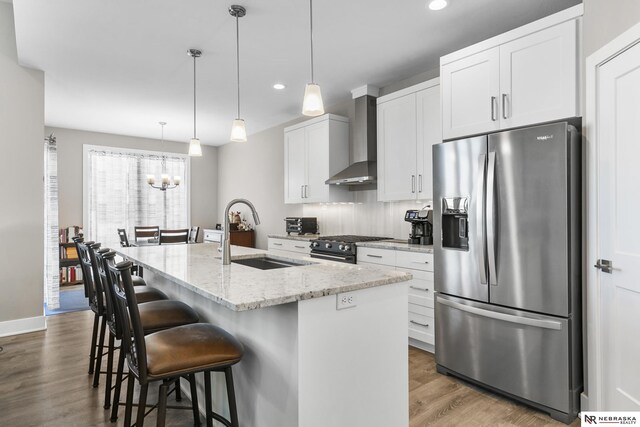 kitchen featuring stainless steel fridge, a sink, wall chimney exhaust hood, wood finished floors, and recessed lighting