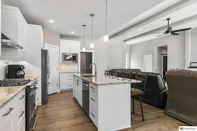 kitchen featuring stainless steel appliances, a sink, wall chimney exhaust hood, a breakfast bar, and open floor plan