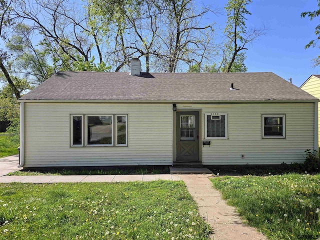 ranch-style home featuring a chimney, a front lawn, and a shingled roof