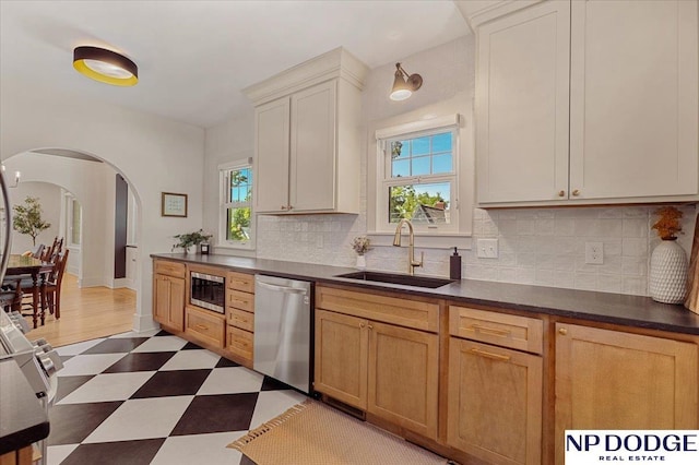 5650 Poppleton Ave, Omaha, NE 68106 - kitchen with appliances with stainless steel finishes, a sink, arched walkways, tile patterned floors, and dark countertops
