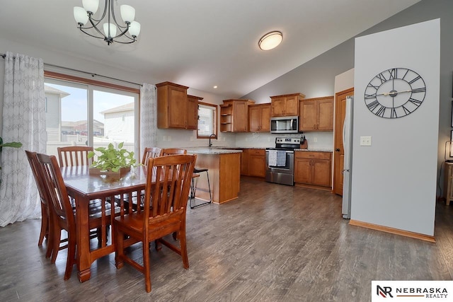 kitchen featuring appliances with stainless steel finishes, vaulted ceiling, brown cabinets, a chandelier, and dark wood finished floors