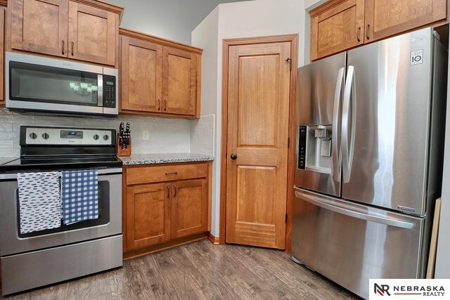 kitchen featuring stainless steel appliances, dark wood-style flooring, tasteful backsplash, brown cabinetry, and light stone countertops