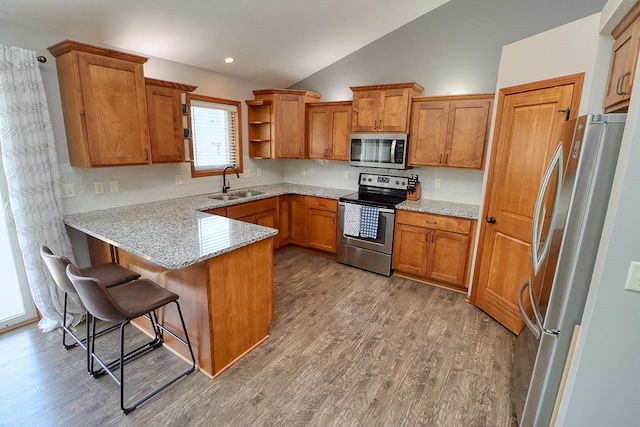 kitchen with appliances with stainless steel finishes, a peninsula, a sink, brown cabinets, and lofted ceiling