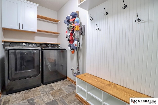 clothes washing area with separate washer and dryer, cabinet space, stone finish floors, and baseboards