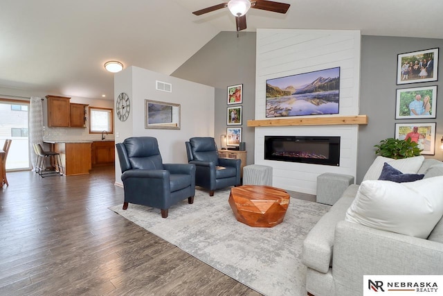 living room featuring lofted ceiling, wood finished floors, ceiling fan, and a glass covered fireplace