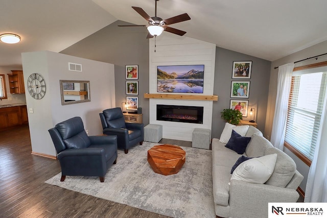 living room featuring wood finished floors, lofted ceiling, a ceiling fan, a glass covered fireplace, and baseboards