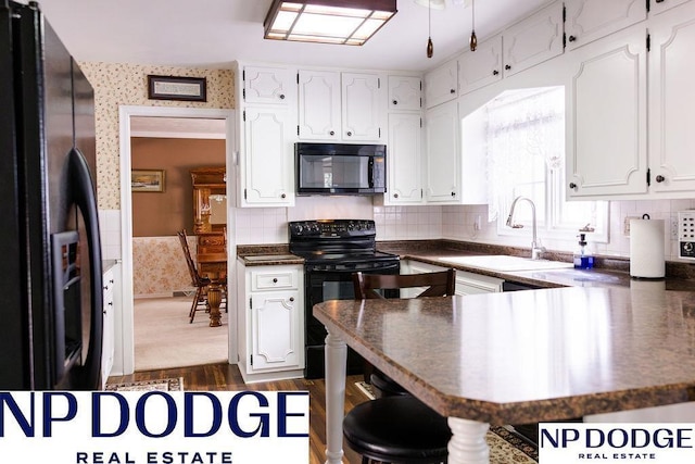 kitchen with black appliances, a sink, dark countertops, wallpapered walls, and white cabinetry