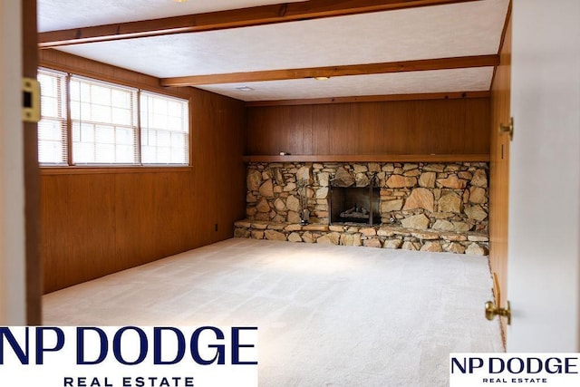 unfurnished living room with beamed ceiling, wooden walls, carpet floors, and a stone fireplace
