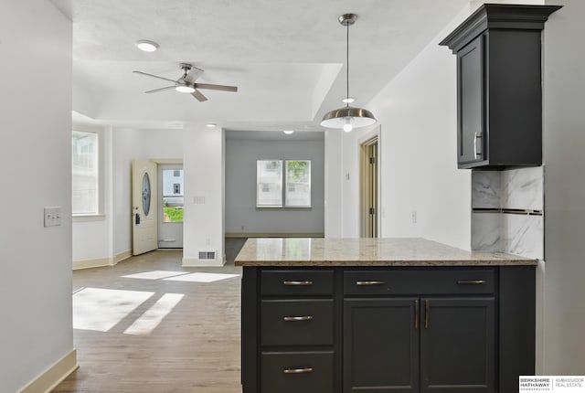 kitchen with a ceiling fan, baseboards, light wood finished floors, and a raised ceiling