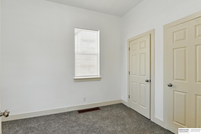 unfurnished room featuring dark colored carpet and baseboards