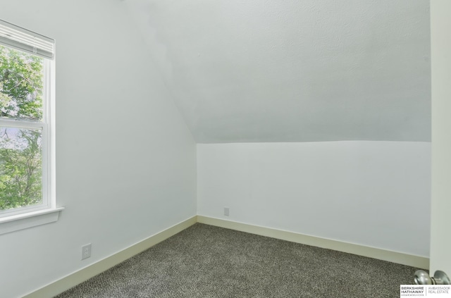 additional living space with dark carpet, vaulted ceiling, and baseboards