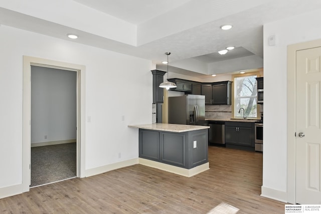 kitchen featuring appliances with stainless steel finishes, a sink, a tray ceiling, light wood-style flooring, and recessed lighting