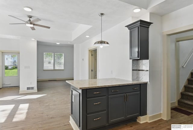 kitchen featuring backsplash, light wood-style flooring, a ceiling fan, decorative light fixtures, and light stone countertops