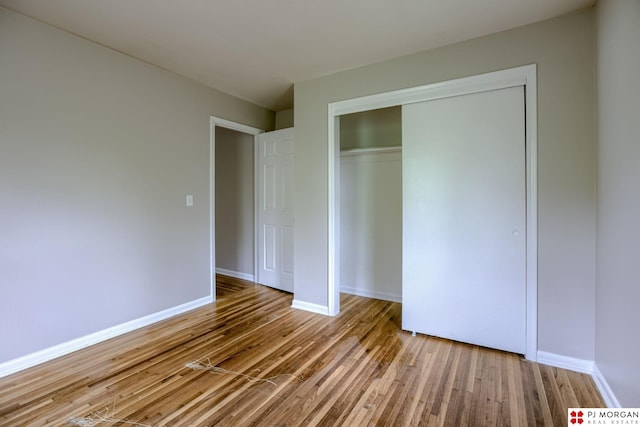 unfurnished bedroom with wood finished floors, baseboards, and a closet