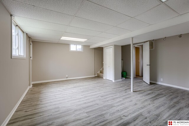below grade area featuring a paneled ceiling, wood finished floors, baseboards, and stairway