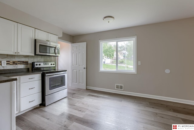 kitchen featuring appliances with stainless steel finishes, dark countertops, light wood-style flooring, baseboards, and white cabinets