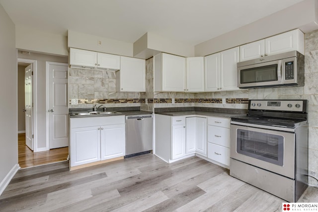 kitchen featuring stainless steel appliances, a sink, tasteful backsplash, dark countertops, and white cabinets
