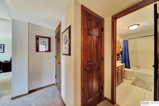 hallway featuring a textured ceiling, light carpet, baseboards, and light tile patterned floors