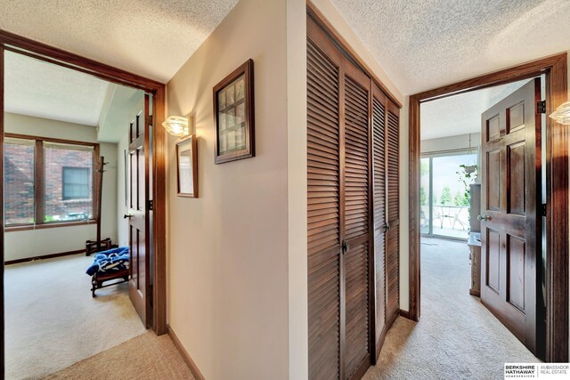 hall with light colored carpet, a textured ceiling, and baseboards