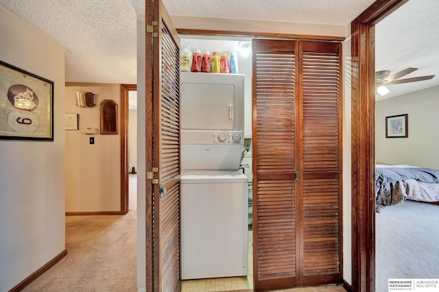 clothes washing area featuring stacked washing machine and dryer, carpet flooring, a textured ceiling, baseboards, and ceiling fan