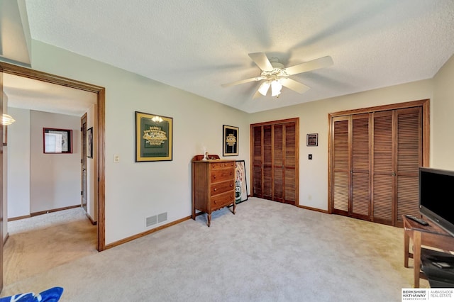 bedroom featuring multiple closets, light colored carpet, a textured ceiling, ceiling fan, and baseboards