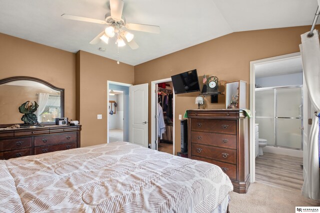 carpeted bedroom featuring a spacious closet, a closet, lofted ceiling, ensuite bathroom, and a ceiling fan