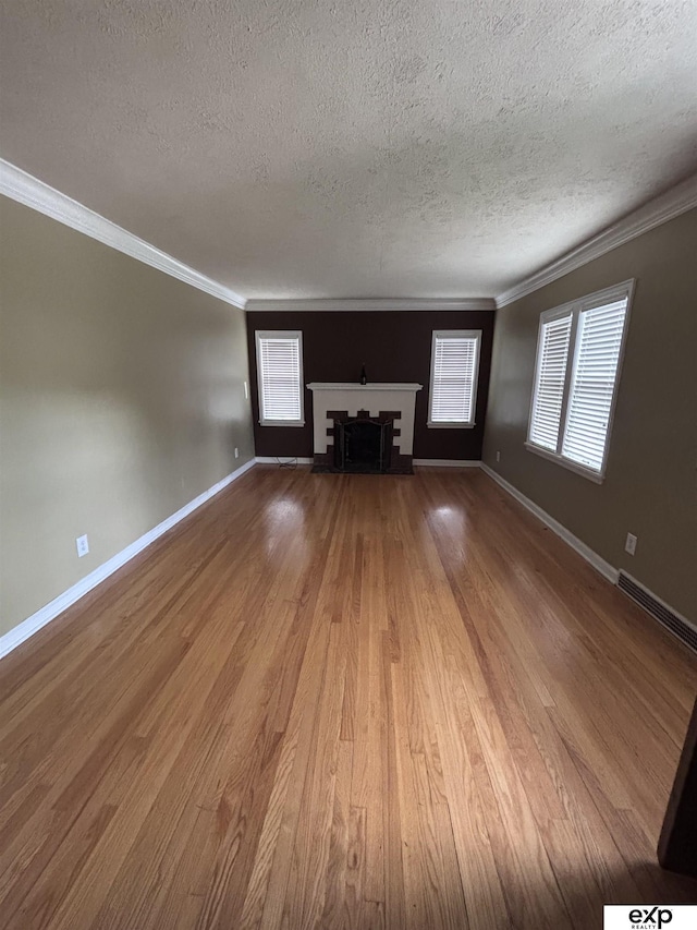 unfurnished living room with a textured ceiling, wood finished floors, crown molding, a fireplace, and baseboards
