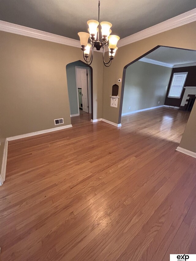 unfurnished dining area featuring arched walkways, a chandelier, crown molding, wood finished floors, and baseboards
