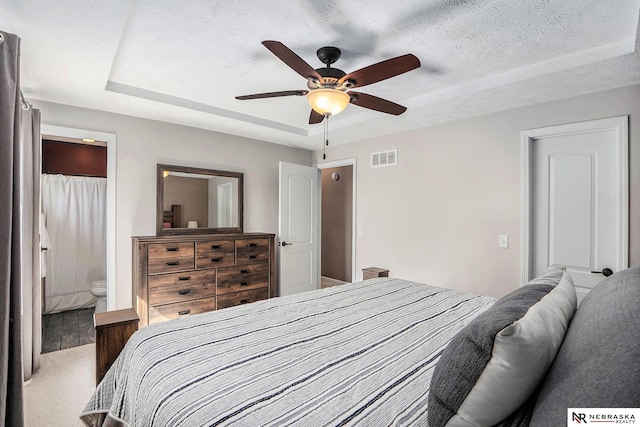 bedroom featuring a raised ceiling, carpet floors, a textured ceiling, a ceiling fan, and connected bathroom