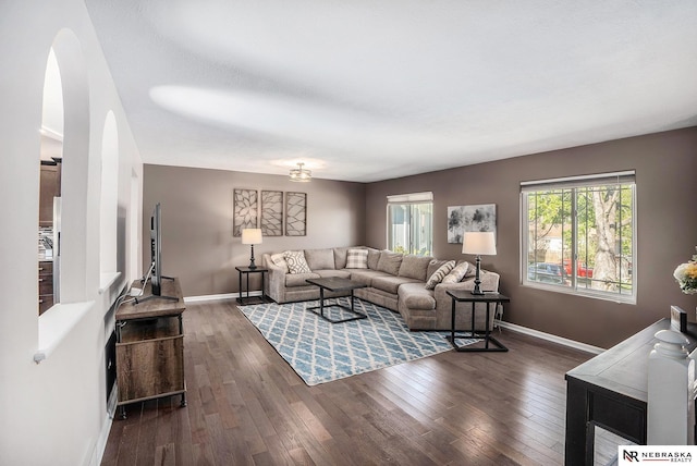 living room with arched walkways, baseboards, and dark wood-style flooring