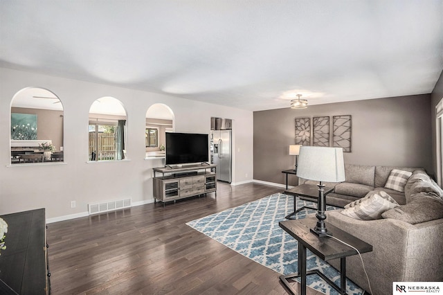 living room with dark wood finished floors, arched walkways, and baseboards