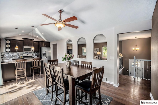 dining room featuring dark wood-style flooring, a ceiling fan, vaulted ceiling, and a chandelier