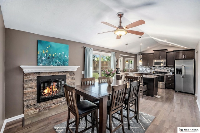 dining room with vaulted ceiling, ceiling fan, wood finished floors, and a fireplace