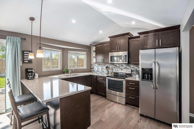 kitchen featuring stainless steel appliances, dark brown cabinets, a peninsula, a sink, and light stone counters