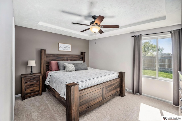 bedroom with a tray ceiling, light carpet, baseboards, a textured ceiling, and ceiling fan