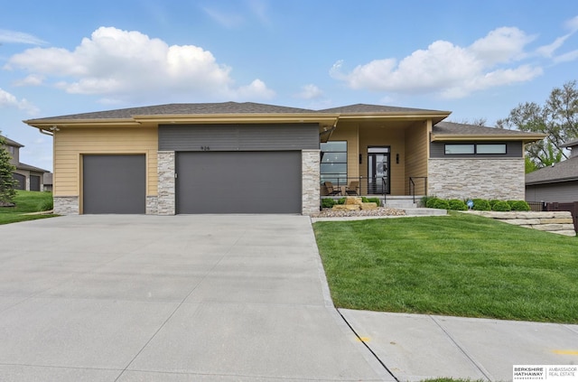 prairie-style house featuring stone siding, an attached garage, a front lawn, and concrete driveway