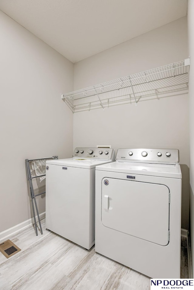 clothes washing area featuring washing machine and clothes dryer, light wood finished floors, and baseboards