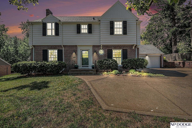 view of front of house with brick siding, asphalt driveway, a lawn, a chimney, and a garage