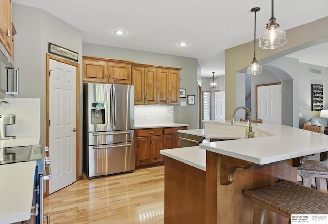 kitchen with appliances with stainless steel finishes, brown cabinets, a sink, a kitchen bar, and recessed lighting