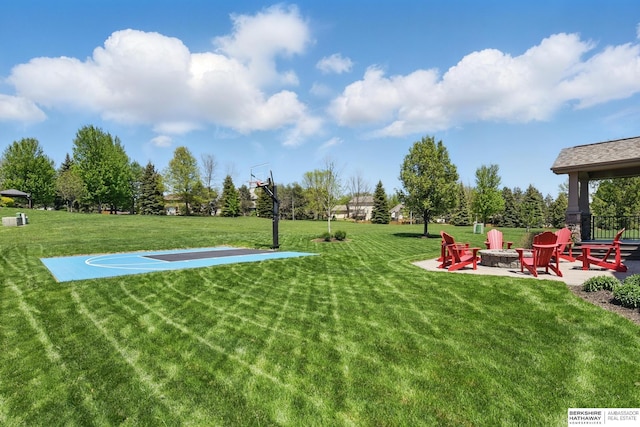 view of green lawn with an outdoor fire pit, community basketball court, and a patio