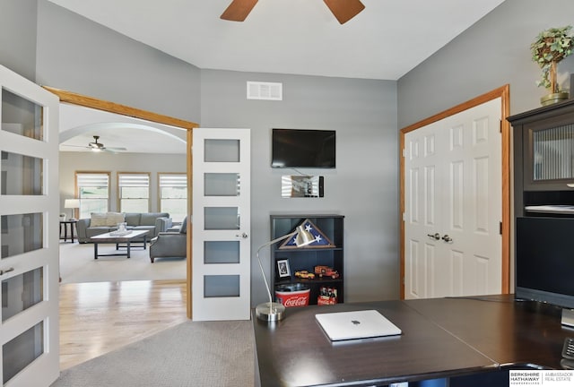 home office with a ceiling fan, arched walkways, and wood finished floors