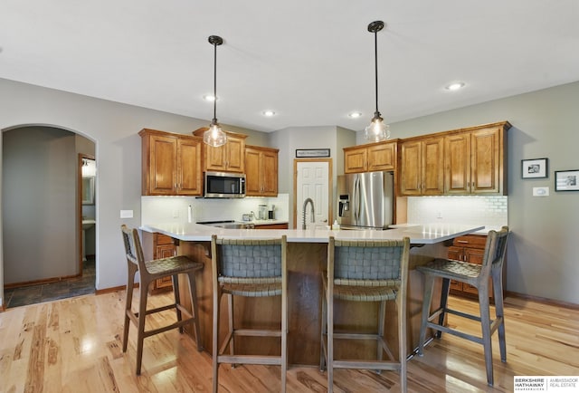 kitchen with stainless steel appliances, arched walkways, light wood-style flooring, tasteful backsplash, and light countertops