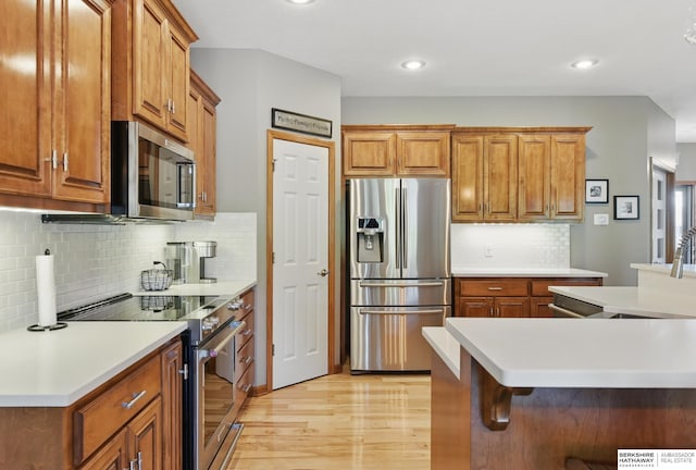 kitchen featuring appliances with stainless steel finishes, light wood-style flooring, brown cabinetry, tasteful backsplash, and light countertops