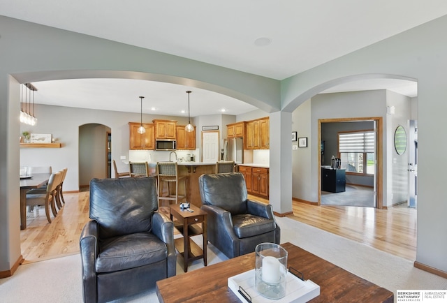 living area with arched walkways, baseboards, light colored carpet, light wood-type flooring, and recessed lighting