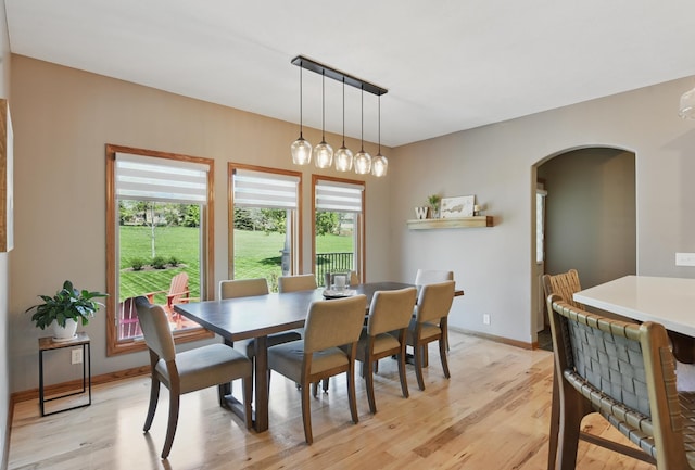 dining space with arched walkways, light wood-type flooring, and plenty of natural light