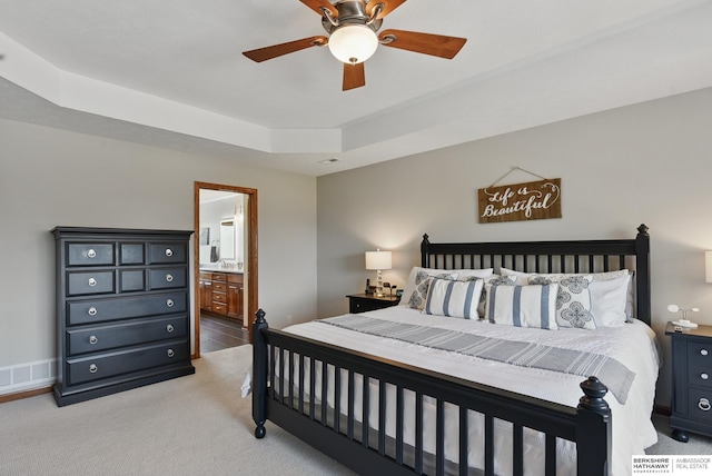 bedroom featuring light carpet, ensuite bathroom, a tray ceiling, and a ceiling fan